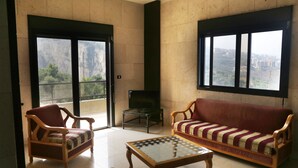 A living room with a sofa, chairs, a glass-top coffee table, and large windows offering a view of a cityscape. - Quiet Comfy and Epic Seaview (Byblos)