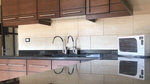 A modern kitchen with dark wooden cabinets, a black countertop, and a stainless steel sink. - Quiet Comfy and Epic Seaview (Byblos)