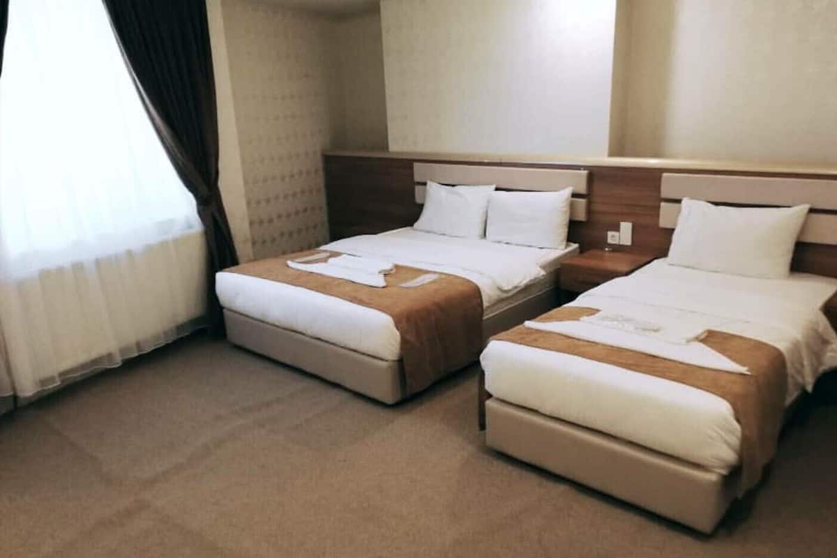 A hotel room with two beds, a wooden headboard, and a large window with curtains.