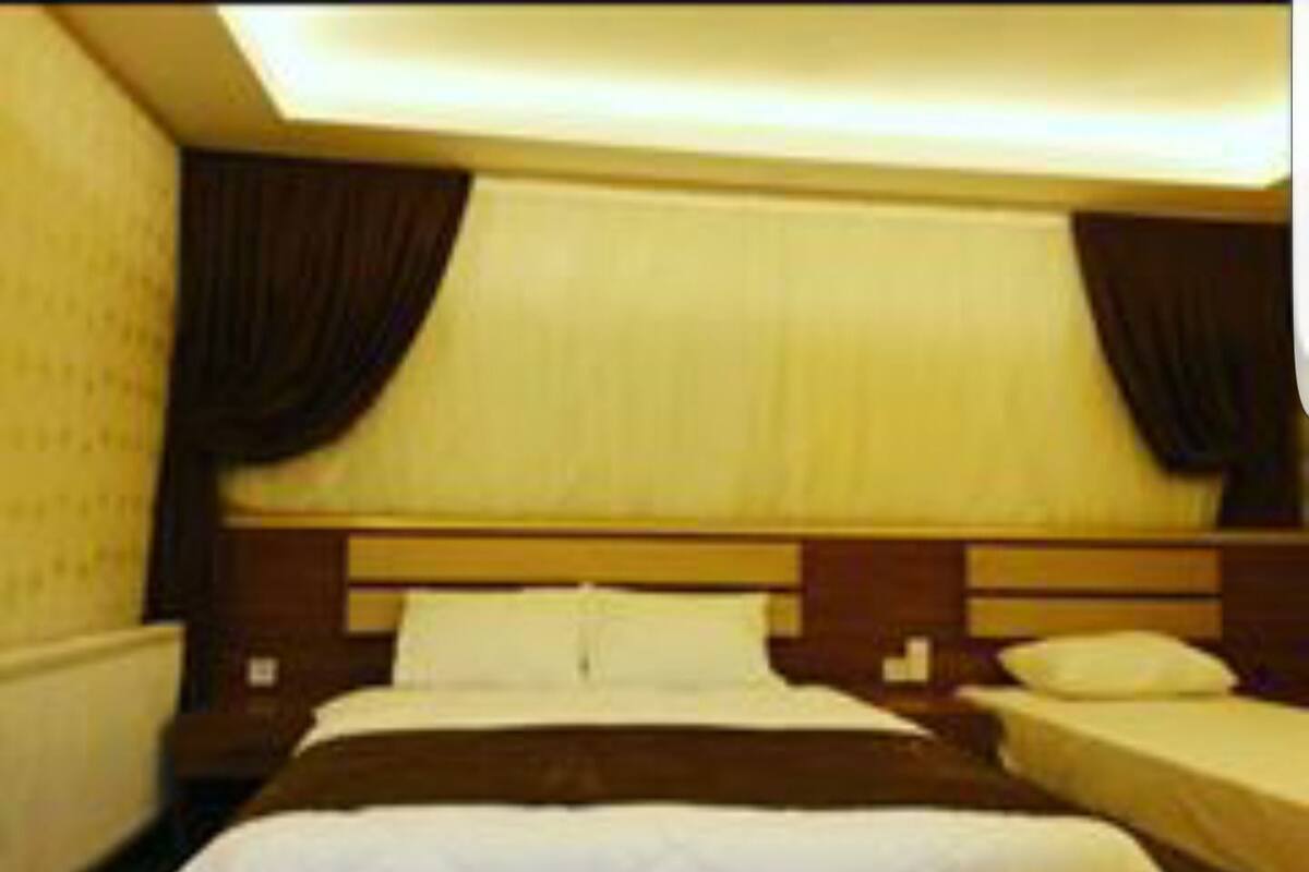 A hotel room with a large bed, two bedside tables, and a headboard with built-in lighting.