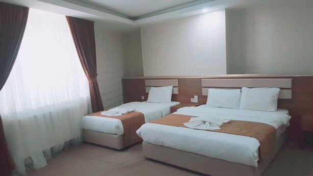 Ein Hotelzimmer mit zwei Betten, einem großen Fenster mit Vorhängen und einem Teppichboden.