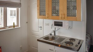 Una cocina compacta con armarios de madera, un microondas integrado y un lavamanos.