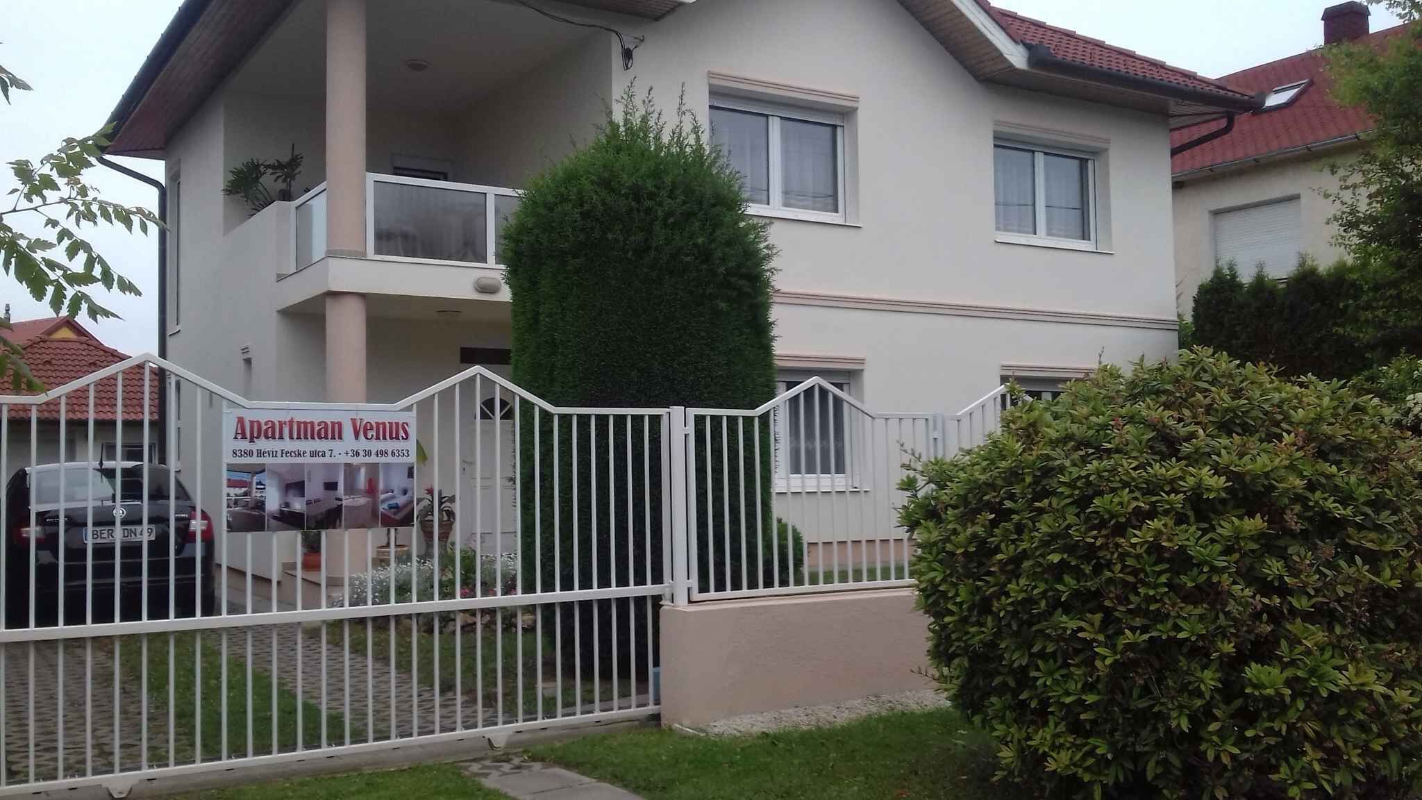 A two-story building with a balcony on the upper floor, a white fence, and a sign advertising 'Apartman Venus'.