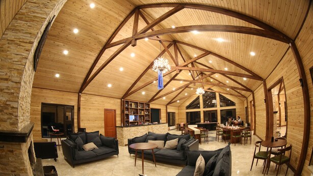 A spacious living area with a high wooden ceiling, a fireplace, sofas, a coffee table, and a dining area with chairs and a table. - Mandala Bliss Mongolia (Ulaanbaatar)