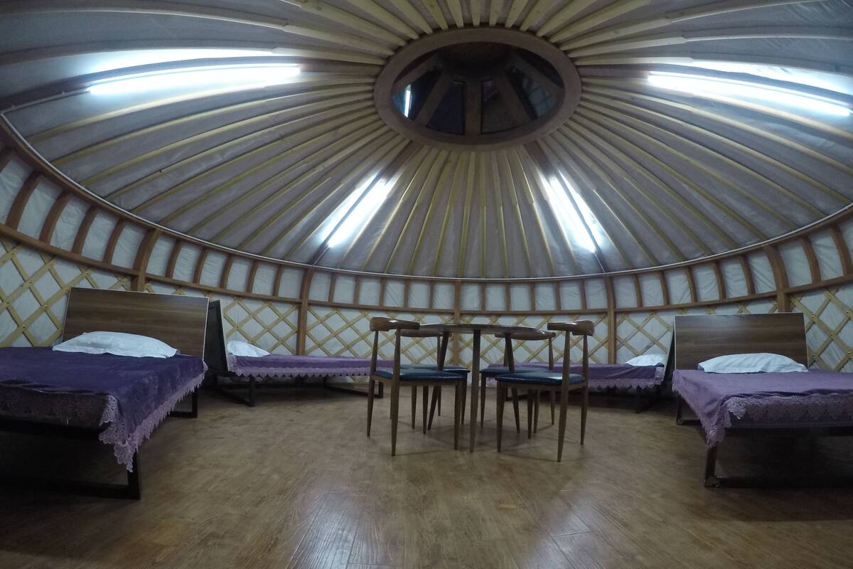 A yurt with four beds, a central table, and chairs.