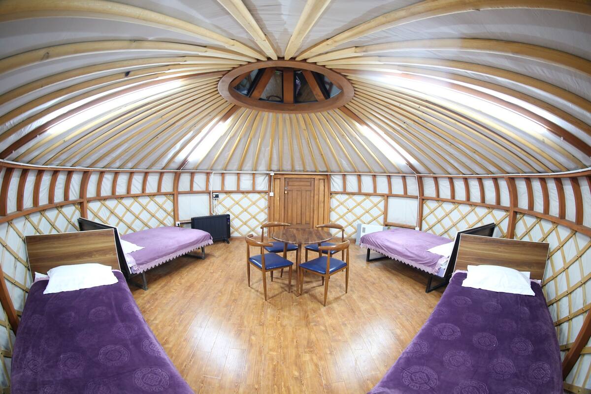 A yurt with four beds, a central wooden table, and a circular skylight.
