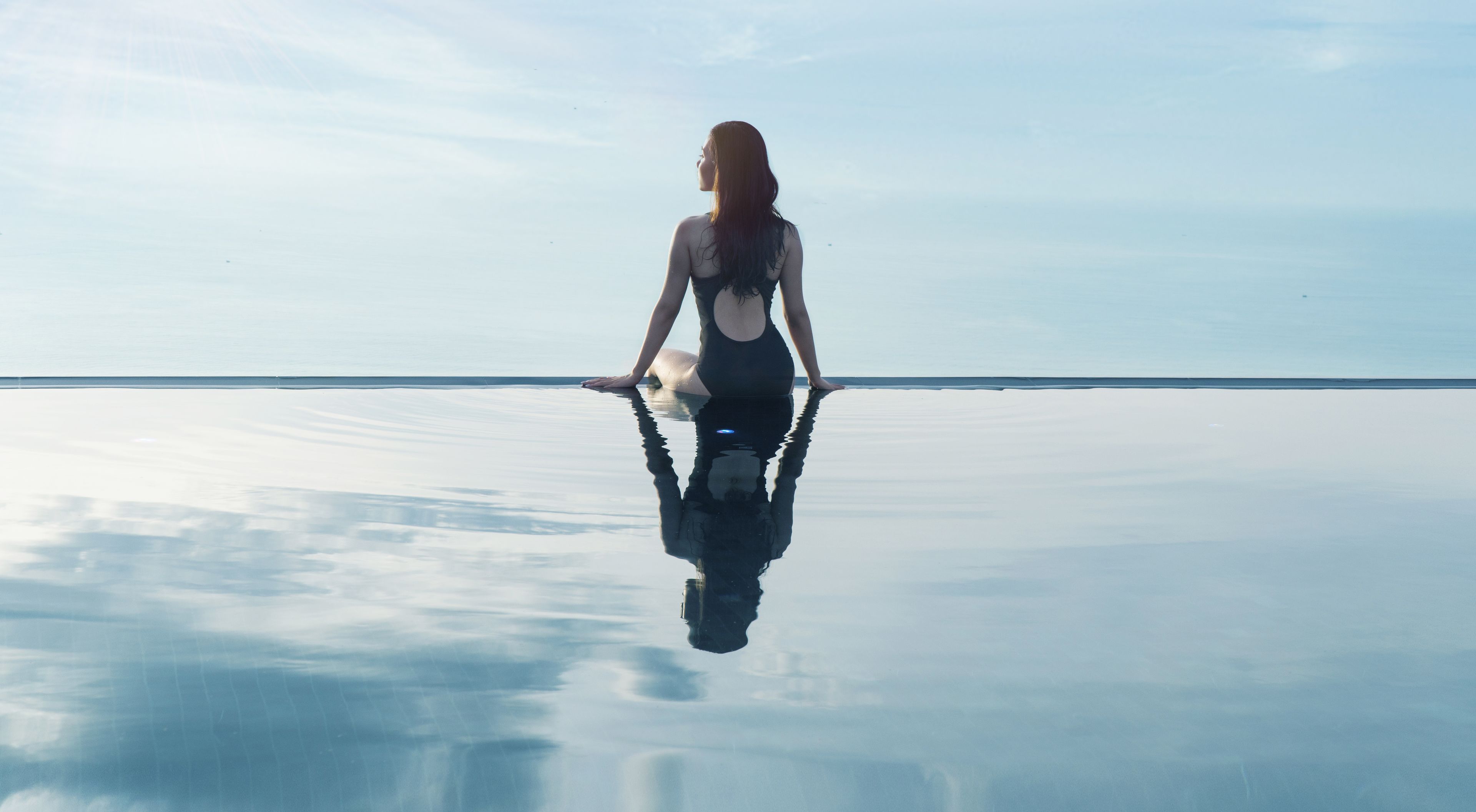 A person sitting on a reflective surface with a clear sky in the background.