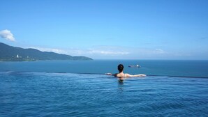 Uma pessoa relaxando em uma grande piscina infinita com vista para o mar e montanhas ao longe.