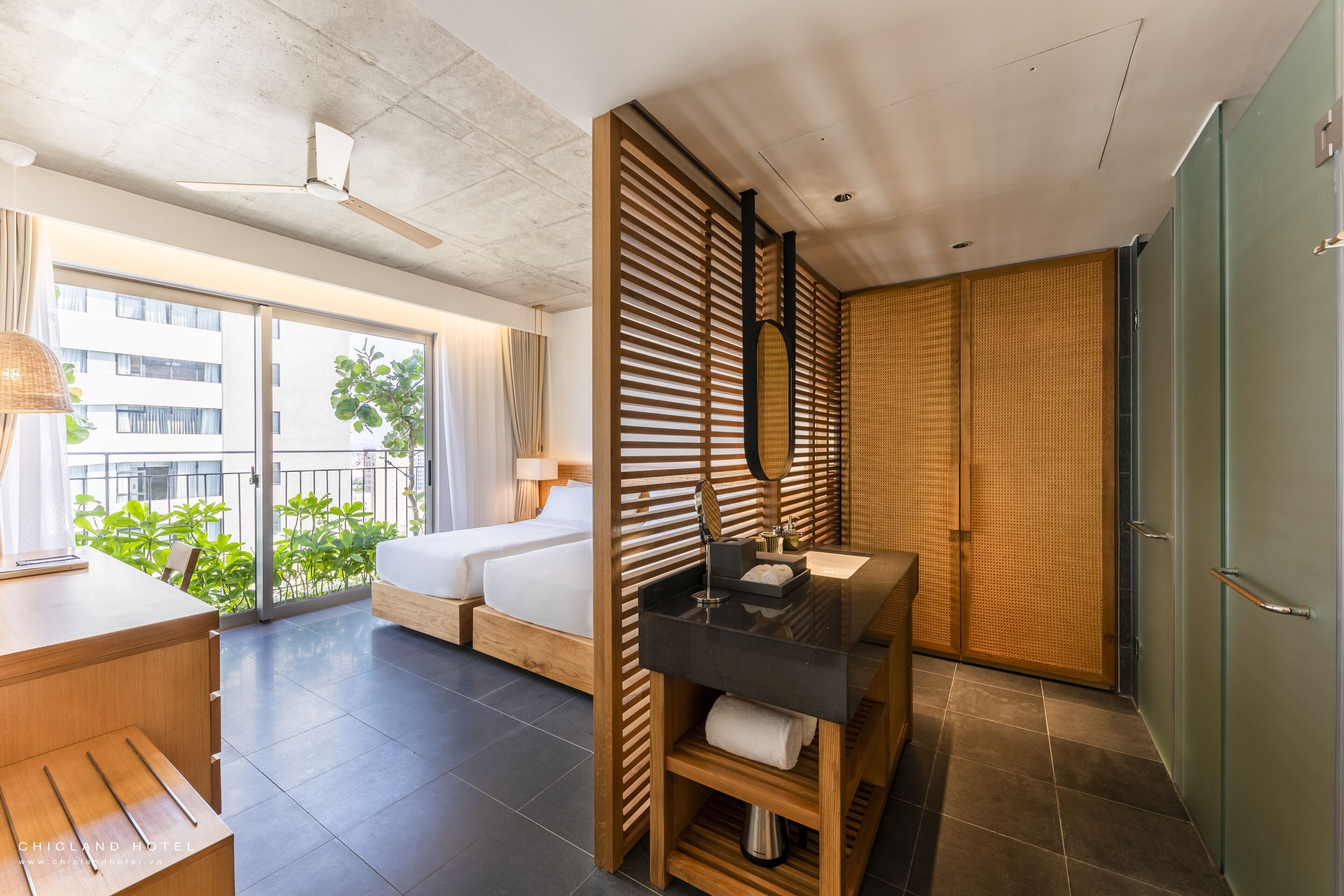 Une chambre d’hôtel avec un lit, un bureau, une salle de bain avec un miroir et une vue sur la verdure.