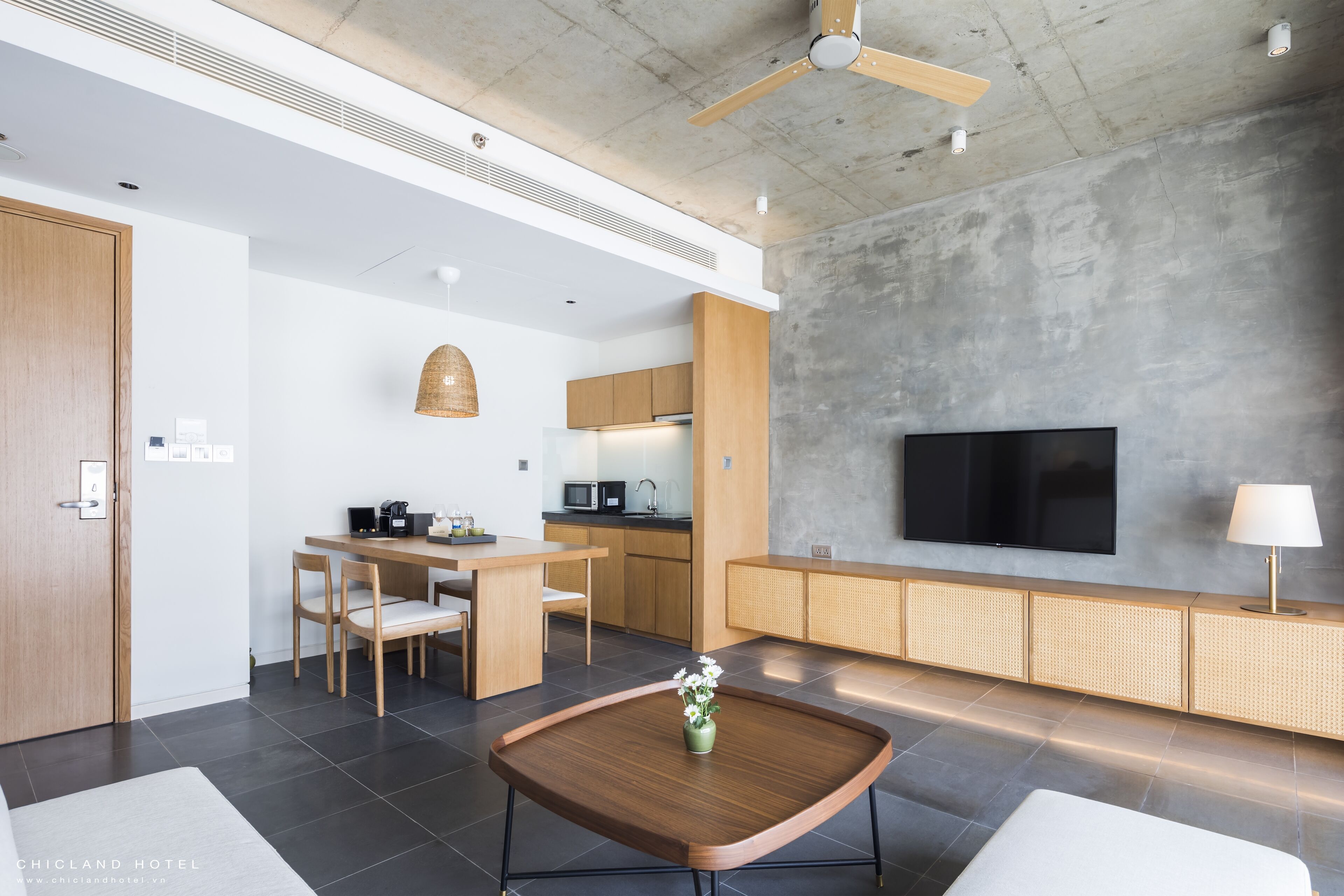 A modern living room with a flat-screen TV, a dining area with wooden furniture, and a kitchen with a microwave and coffee maker.