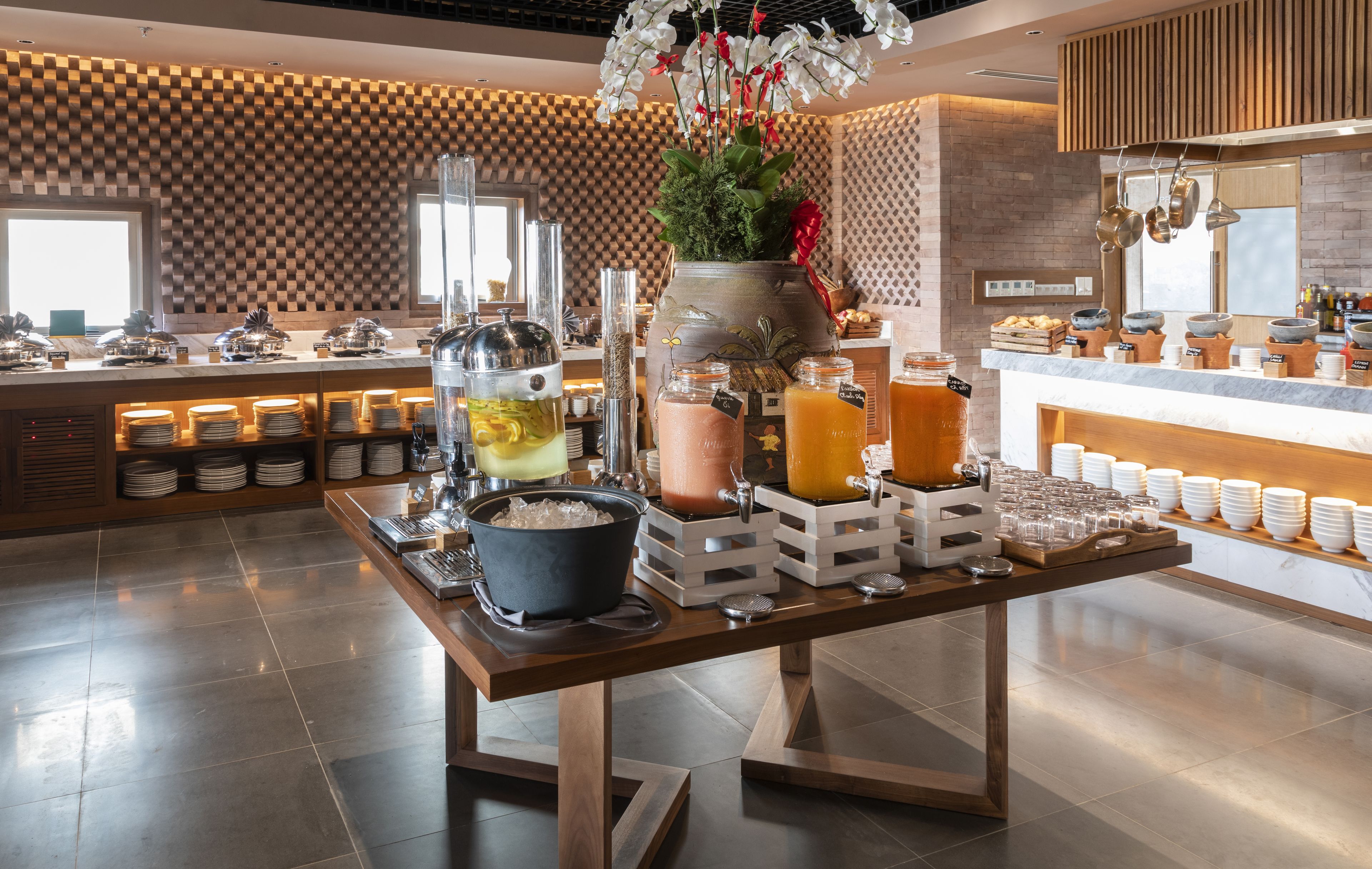 A buffet setup with various food and drink stations, including a fruit display, a beverage station with pitchers, and a counter with bread and pastries.