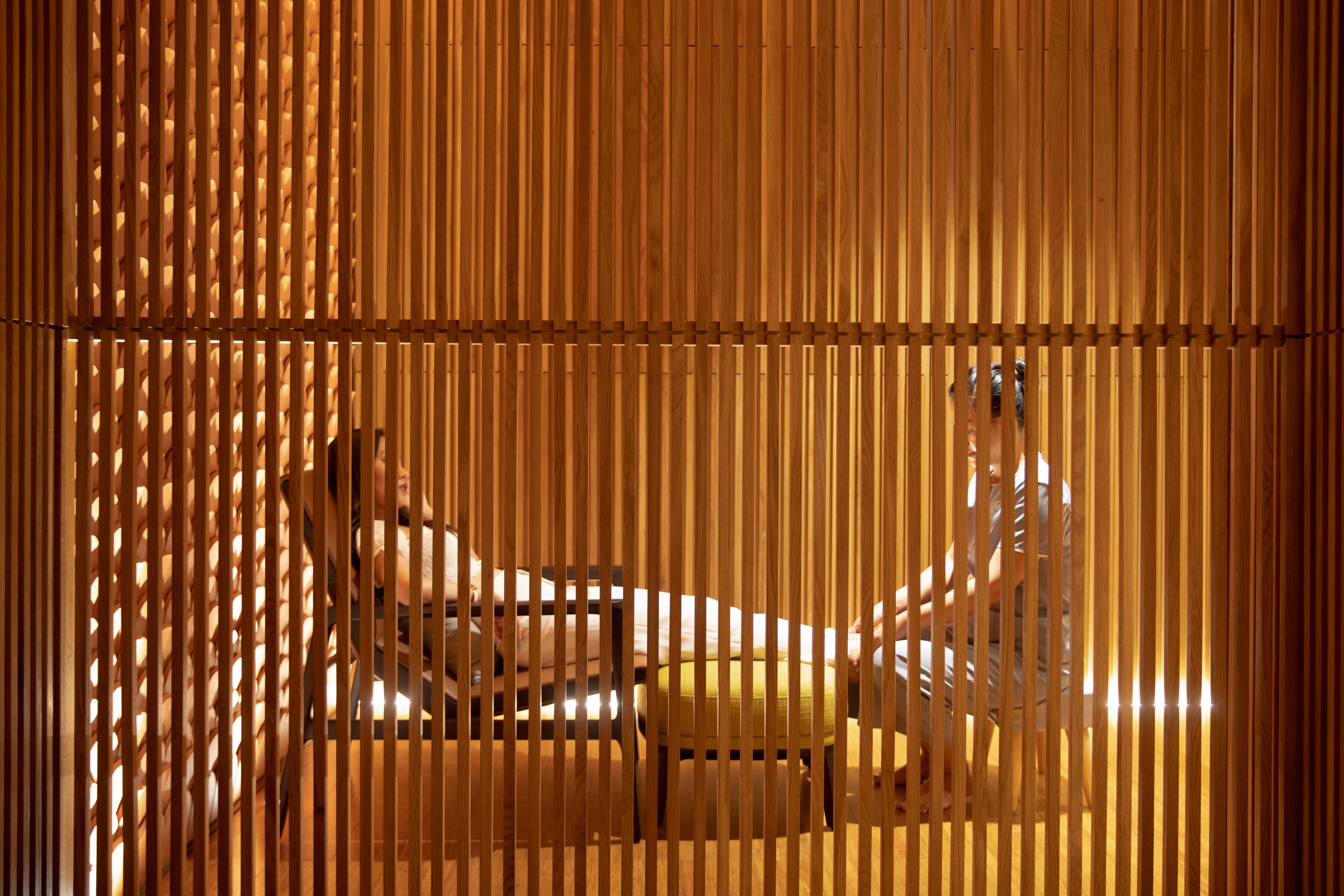 A room with a wooden slat partition, a bed, and a chair.