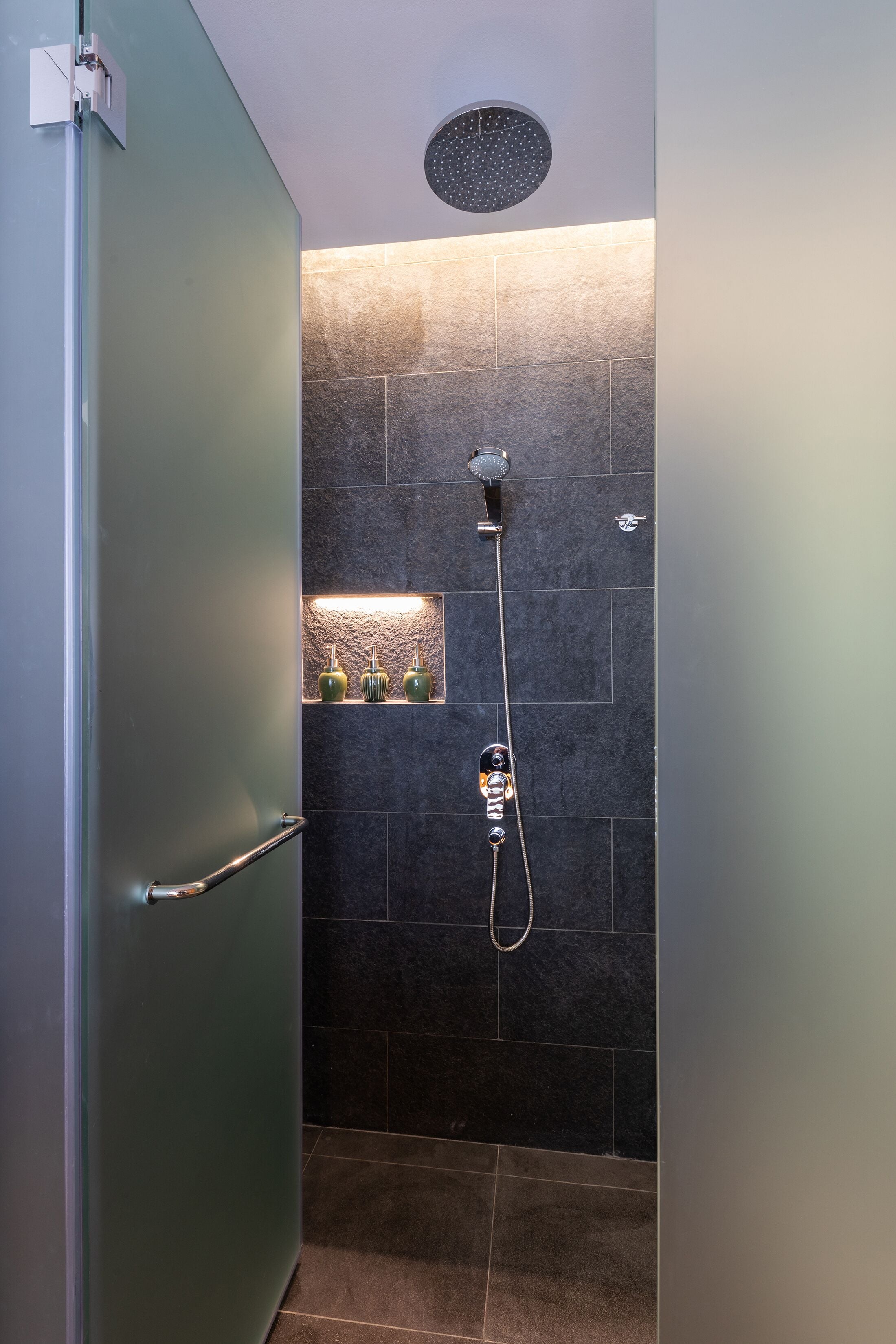 Ein modernes Duschbad mit Handbrause, Wandarmatur und einer Glasablage mit Dekoration.