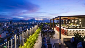 A rooftop bar with outdoor seating, a bar area, and a city view. - Chicland Danang Beach Hotel (Da Nang)