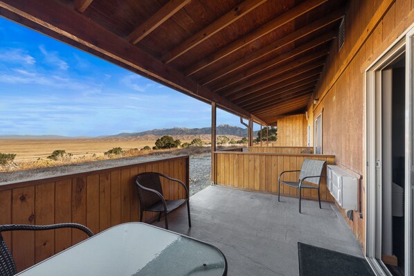 A wooden balcony with two chairs and a table, overlooking a vast landscape with mountains in the distance. - Great Sand Dunes Lodge (Mosca)