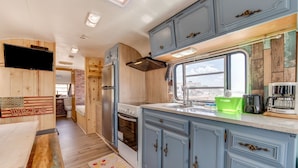 A compact RV kitchen with wooden cabinetry, a built-in oven, and a window providing natural light. - Great Sand Dunes Lodge (Mosca)