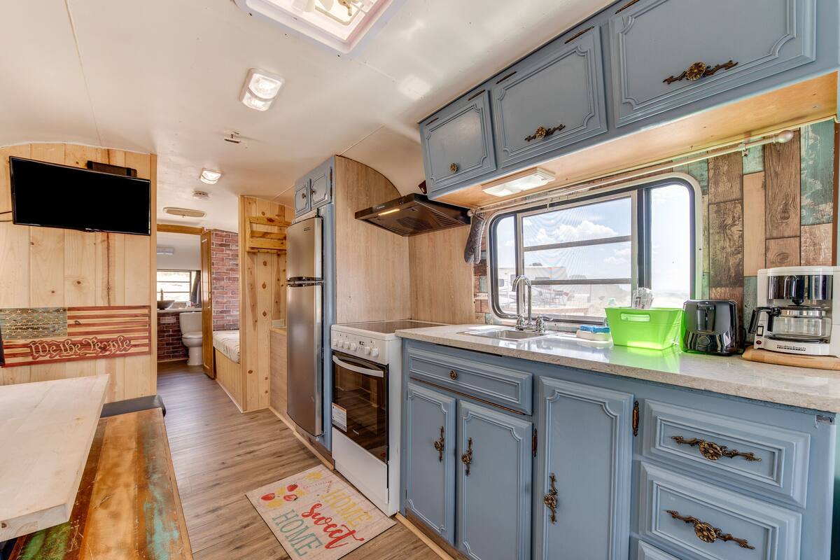 A compact RV kitchen with wooden cabinetry, a built-in oven, and a window providing natural light.