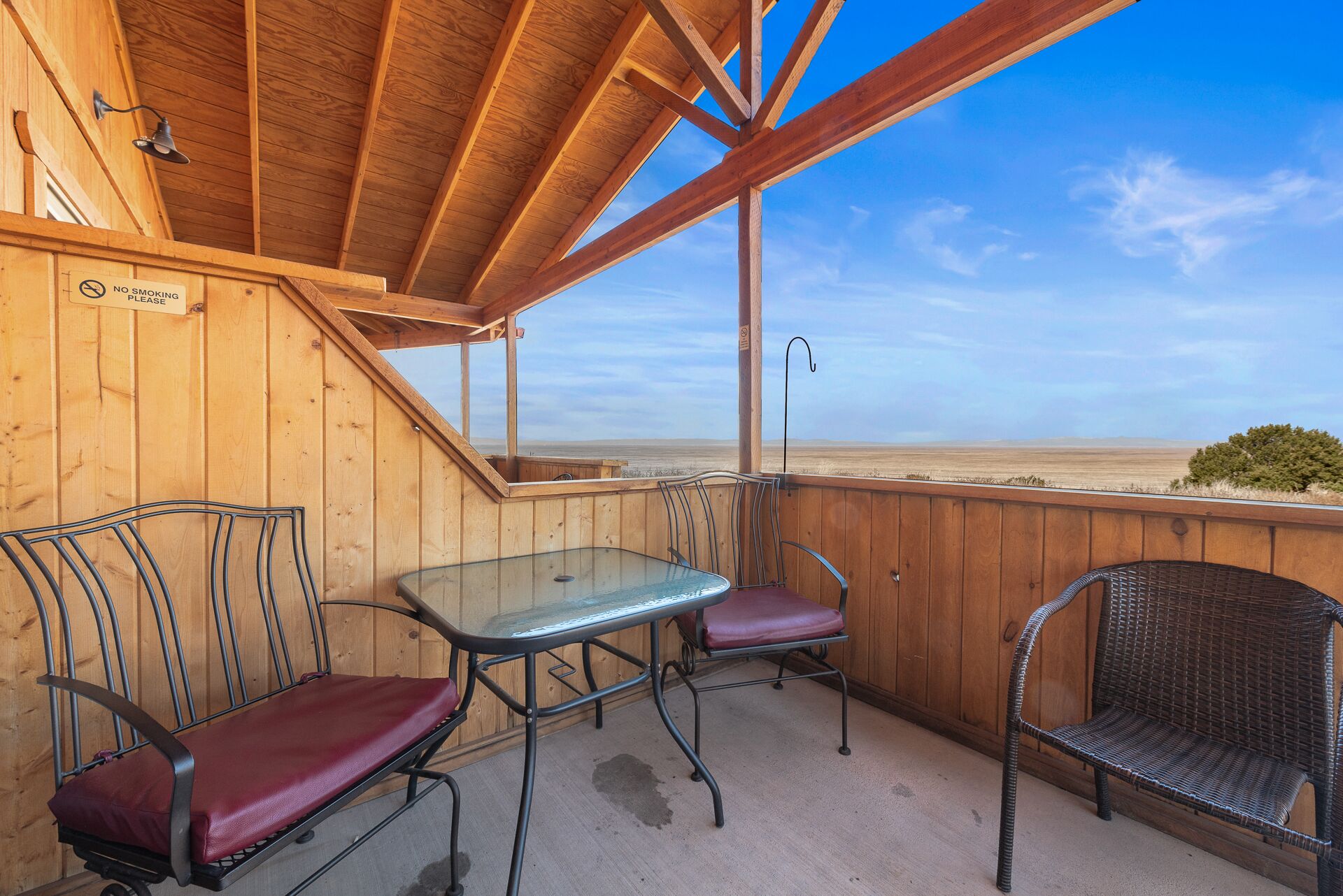 A wooden deck with a glass table and metal chairs, overlooking a beach.