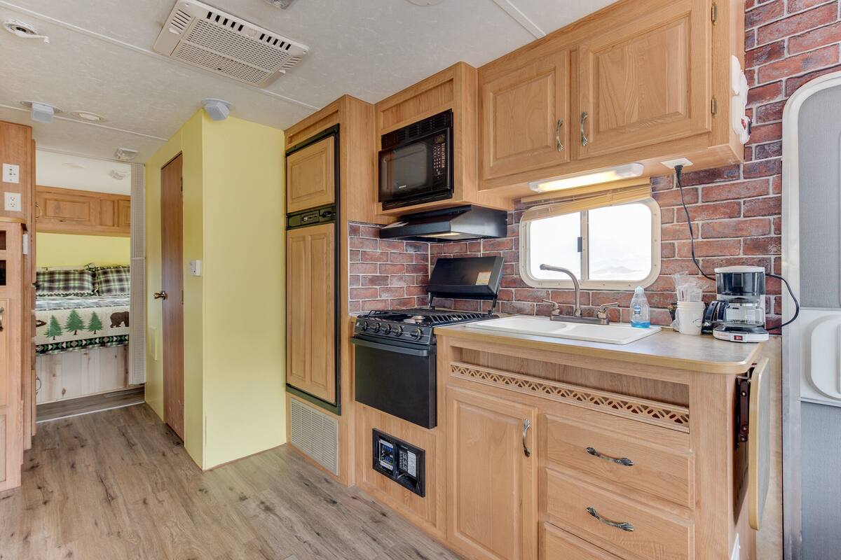 A compact RV kitchen with wooden cabinets, a black stove, a microwave, and a window above the sink.