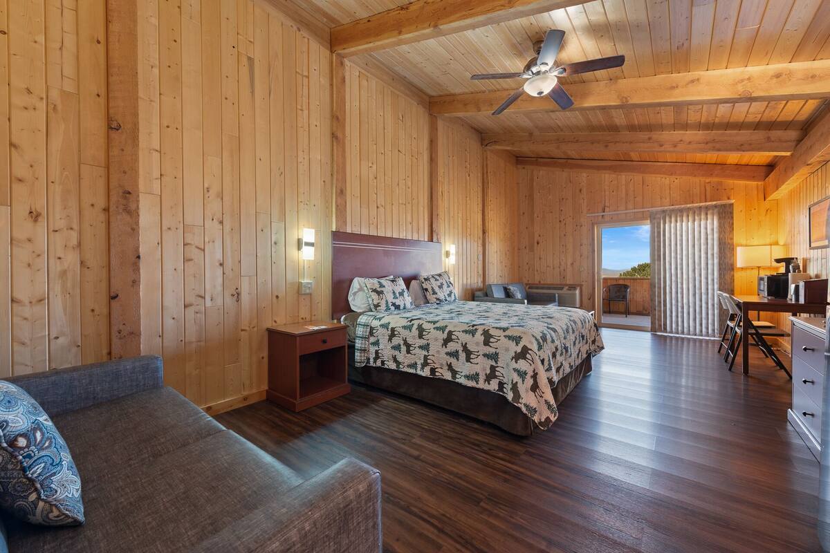 A wooden cabin room with a bed, a desk, and a chair.