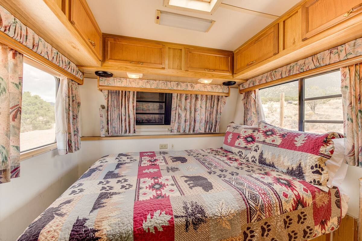 A cozy RV bedroom with a large bed, floral curtains, and a window with a view of the outdoors.