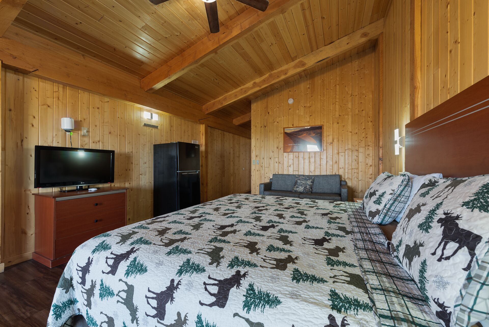 Una habitación de cabaña de madera con una cama, un televisor y un refrigerador.