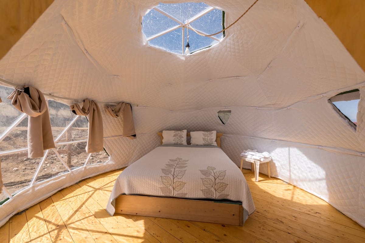 A cozy, tent-like bedroom with a large bed, a small bedside table, and a window.