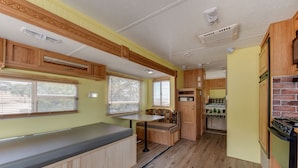 A compact RV kitchen with wooden cabinetry, a built-in stove, and a dining area with a bench. - Great Sand Dunes Lodge (Mosca)
