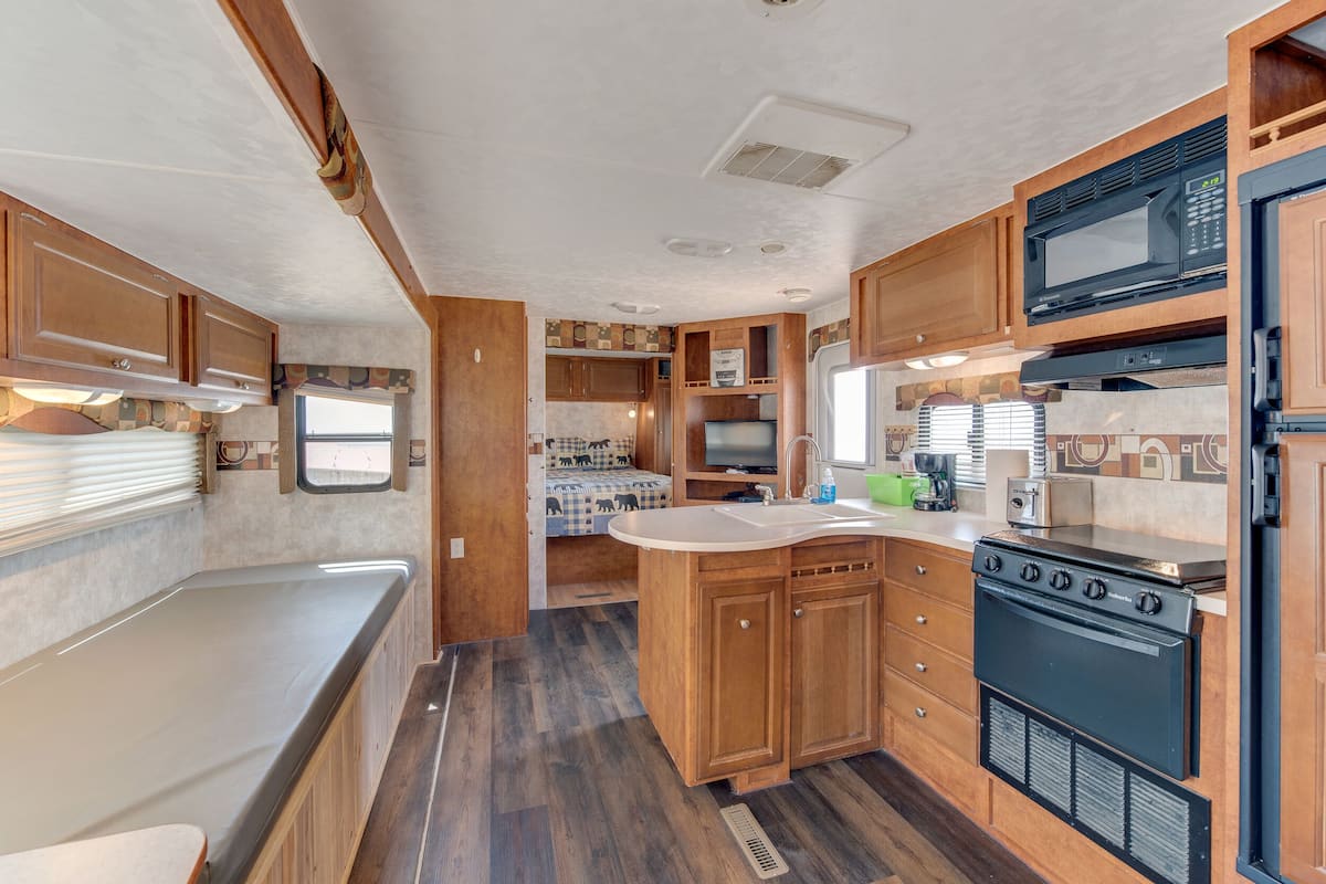 A compact RV kitchen with wooden cabinets, a stove, microwave, and a sink.