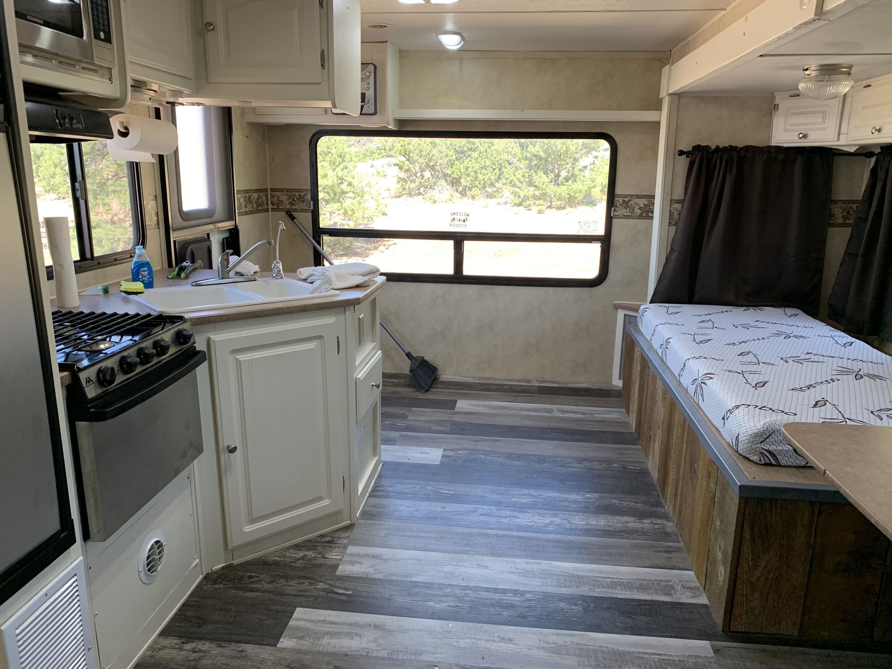 A compact RV kitchen with a gas stove, microwave, sink, and a window providing a view of the outdoors.