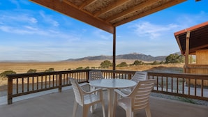 A covered outdoor seating area with a table and chairs, overlooking a mountainous landscape. - Great Sand Dunes Lodge (Mosca)