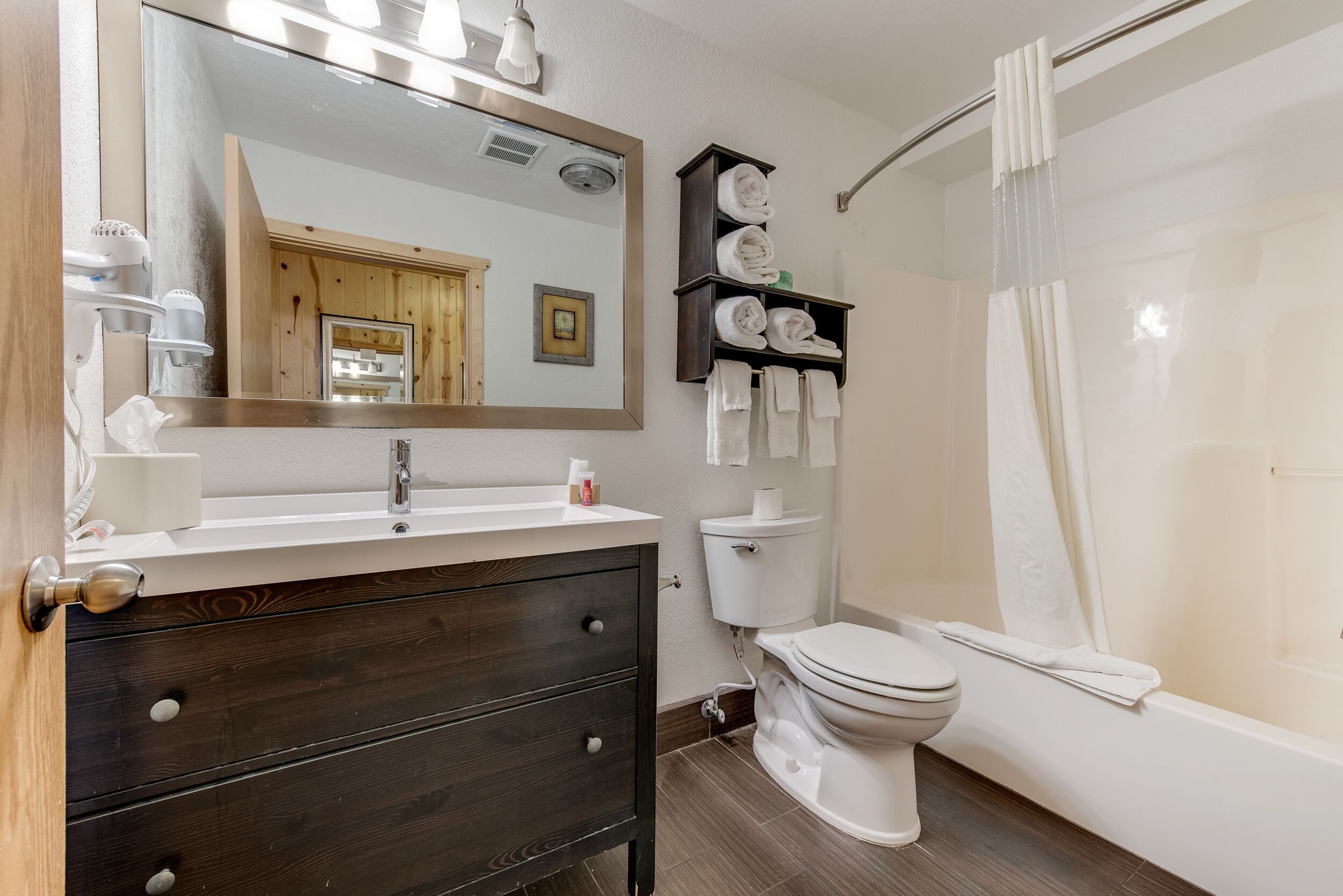 A modern bathroom with a wooden vanity, a toilet, and a shower with a curtain.