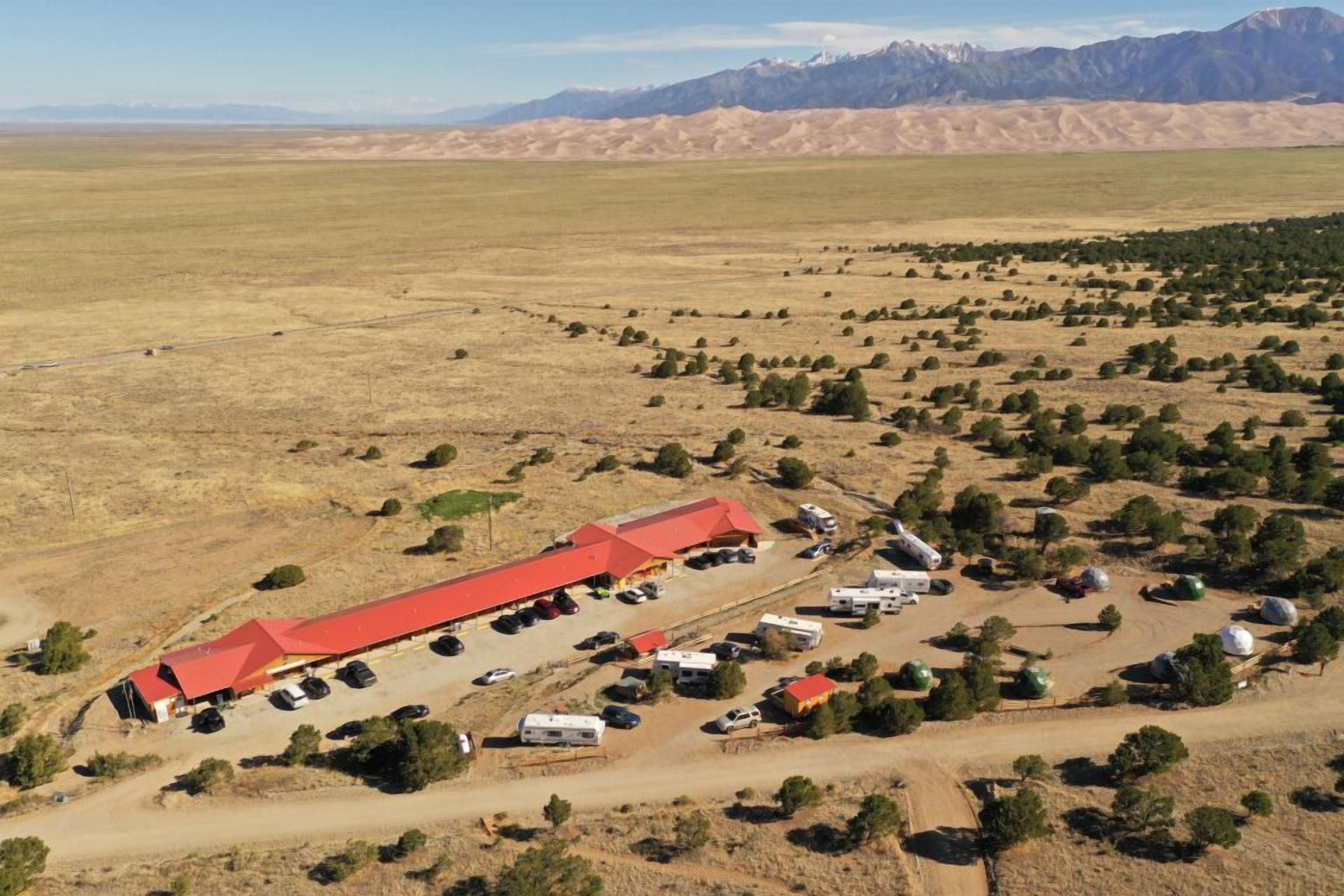 Un parque para vehículos recreativos grande con un edificio rojo, varias casas rodantes y vegetación escasa.