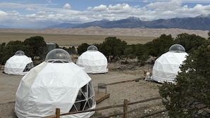 A series of dome-shaped tents with transparent windows, set against a backdrop of mountains and a clear sky. - Great Sand Dunes Lodge (Mosca)