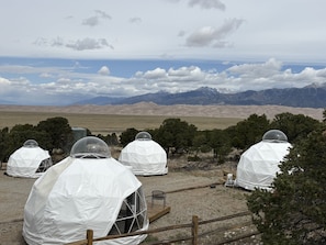 Une série de tentes en forme de dôme, dotées de fenêtres transparentes, se dressent sur fond de montagnes et sous un ciel dégagé.