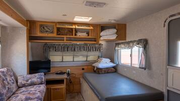 A compact RV interior with a bed, a couch, a TV, and a kitchenette area.