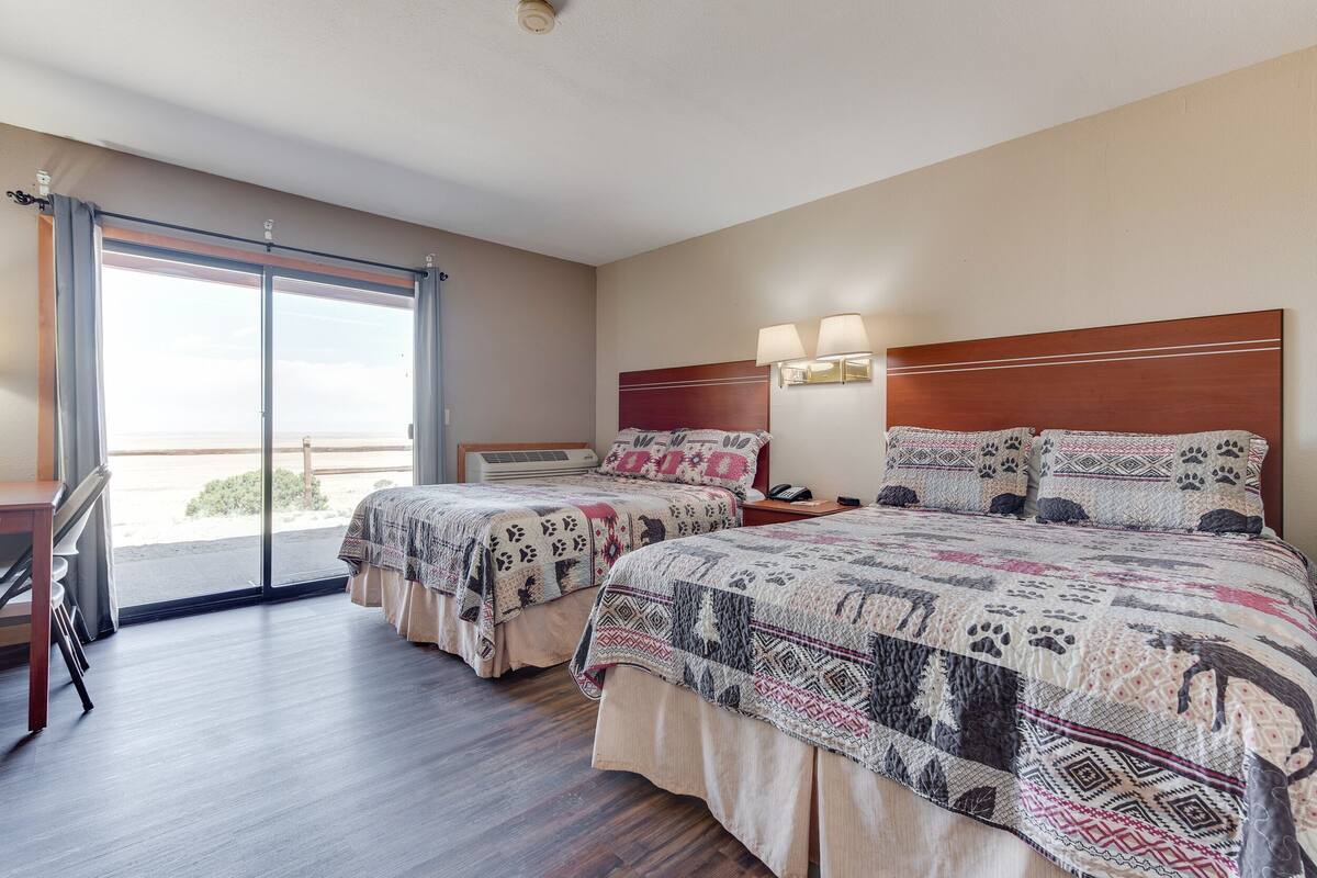 A hotel room with two beds, a desk, and a sliding glass door to the outside.