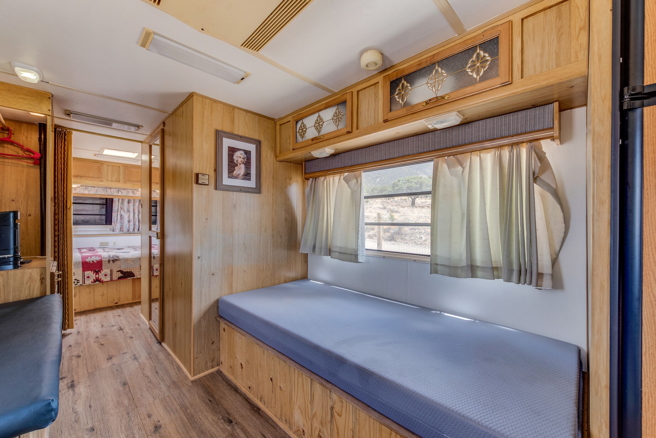 A compact RV interior with a bed, seating area, and a small kitchenette.