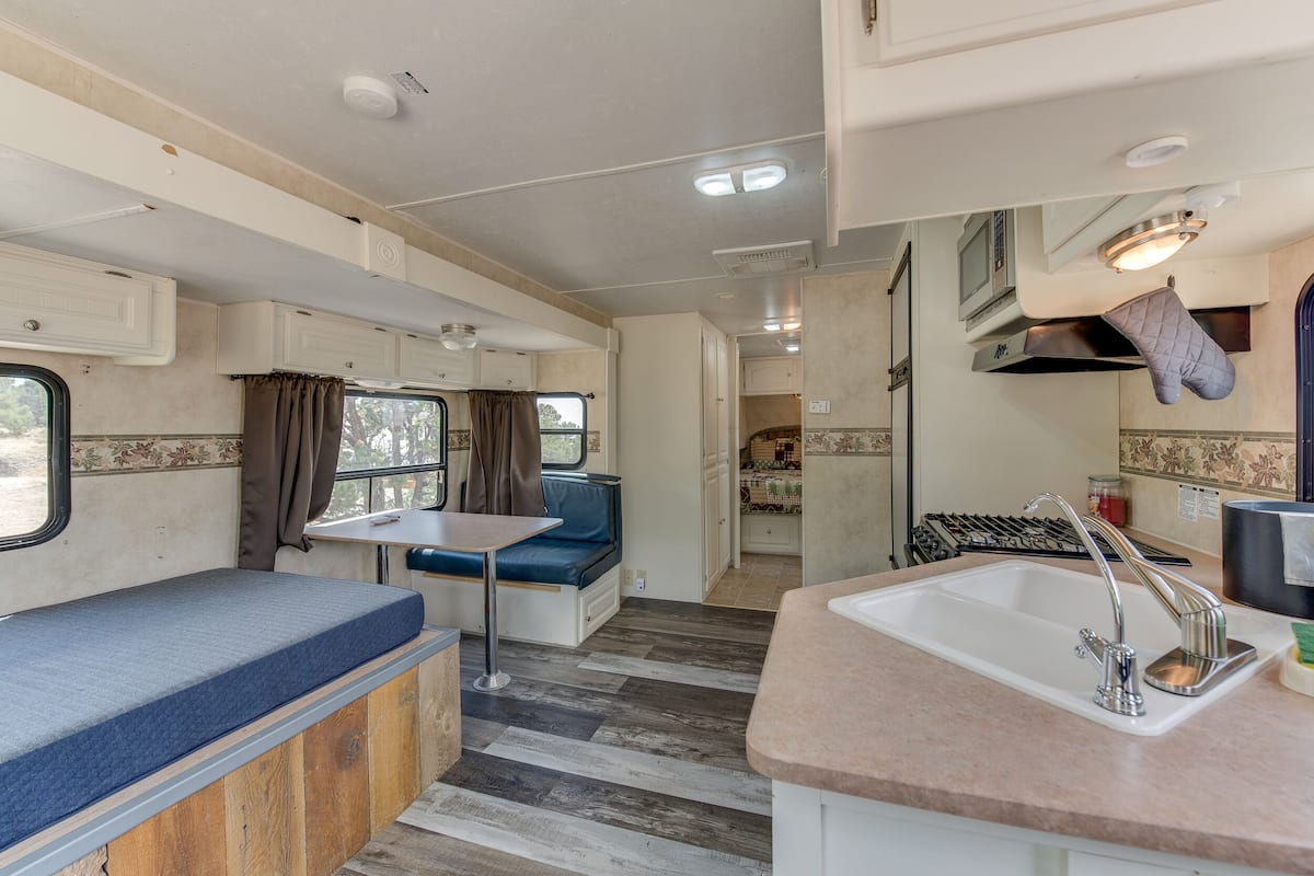A compact RV interior with a kitchenette, a dining area, and a sleeping berth.