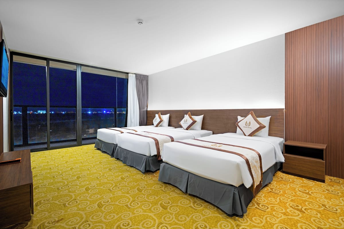 A hotel room with two beds, a large window with a city view, and a yellow patterned carpet.