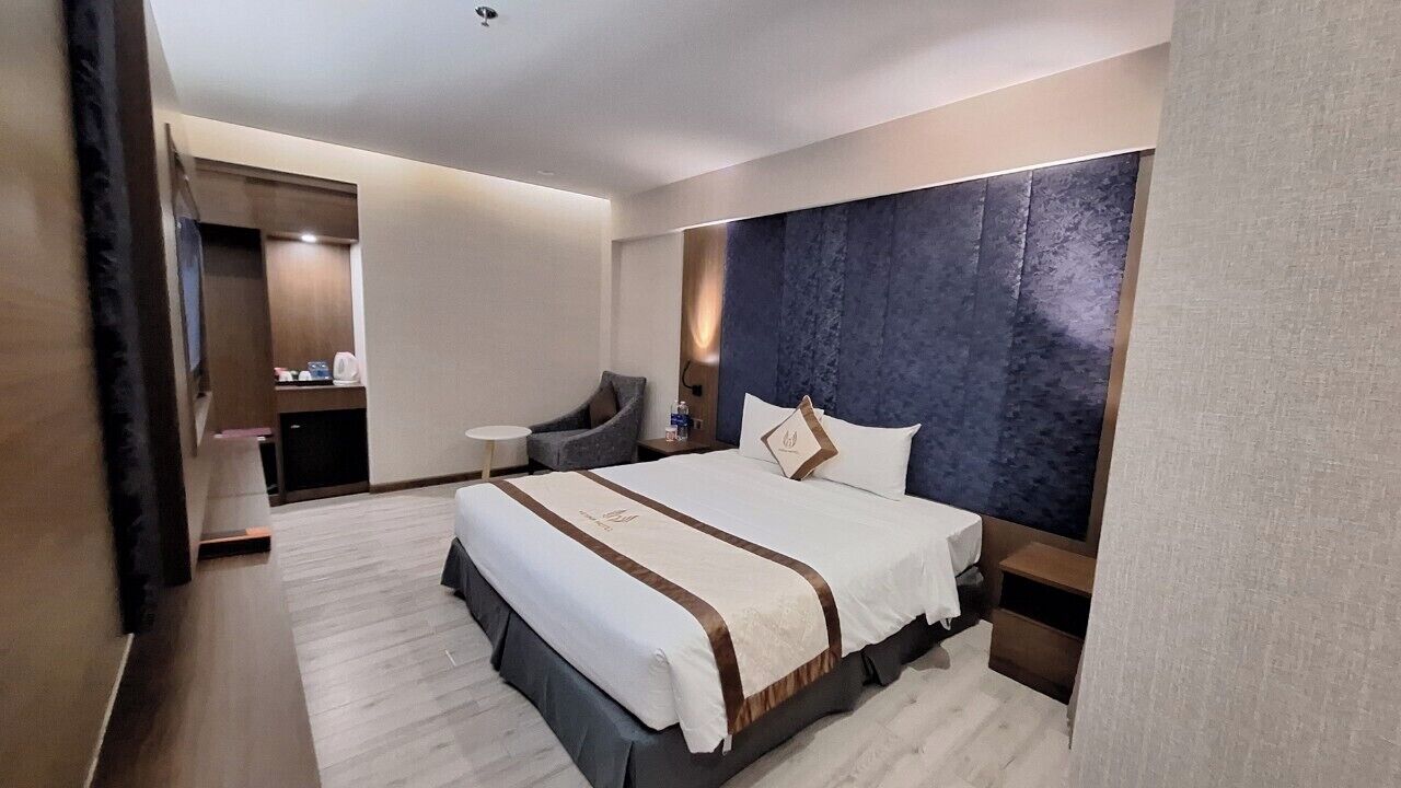 A hotel room with a large bed, a chair, a small table, and a wardrobe.