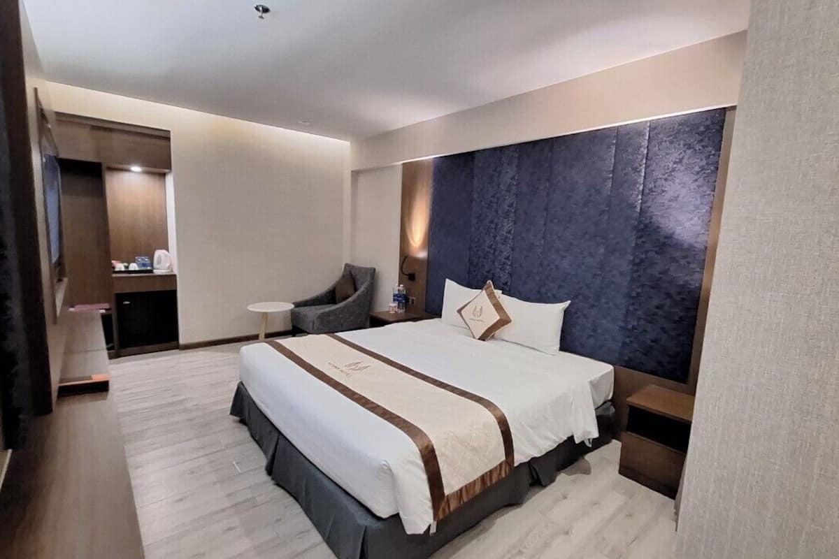 A hotel room with a large bed, a chair, a small table, and a wardrobe.