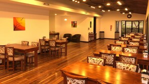 Un vaste espace dédié à la salle à manger, avec des tables et des chaises en bois, un plafond haut avec des poutres apparentes et une vue dégagée grâce à de grandes fenêtres.