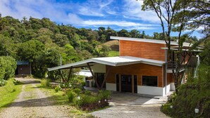 Une maison moderne avec un toit en pente, de grandes fenêtres et une allée pavée menant à l’entrée.