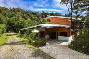 Uma casa moderna com telhado inclinado, grandes janelas e uma entrada com calçada.