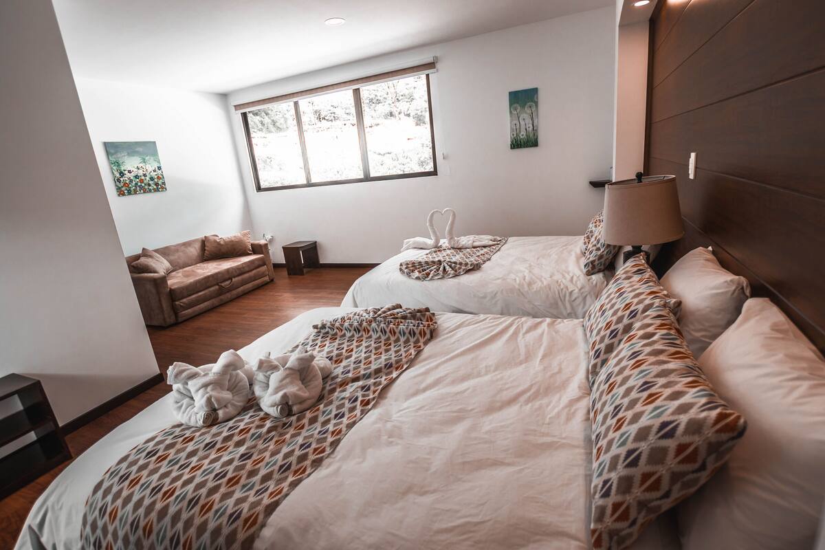 A hotel room with two beds, a sofa, a window, and artwork on the walls.