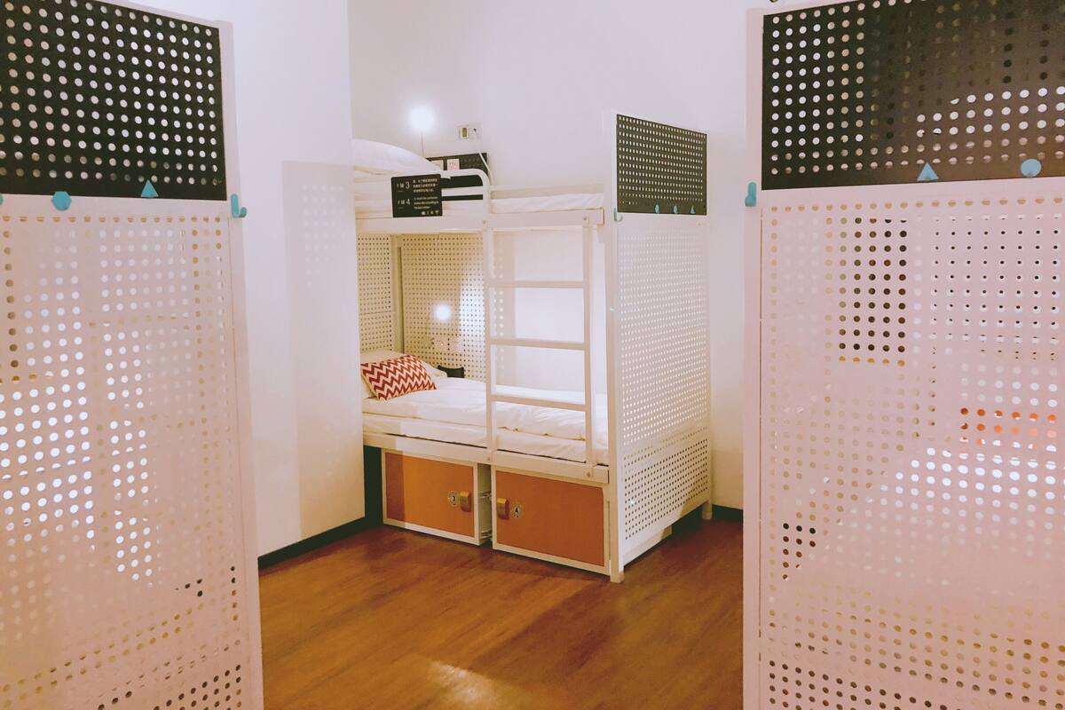 A bunk bed room with a white bed, a nightstand, and a small table. There are two storage boxes under the bed.