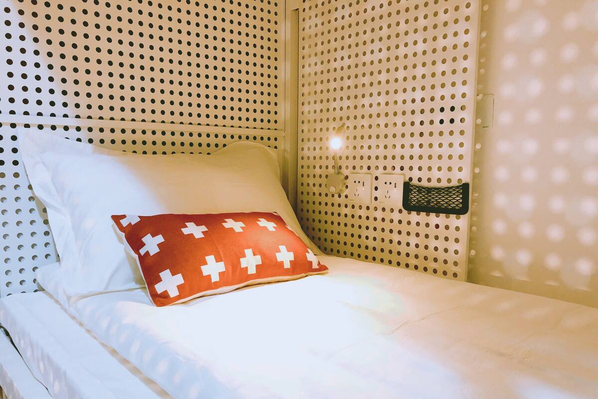 A single bed with white bedding and a red pillow with white crosses.