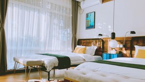 A hotel room with two beds, a wooden headboard, a large window with sheer curtains, a wall-mounted air conditioner, and a cowhide rug on the floor.