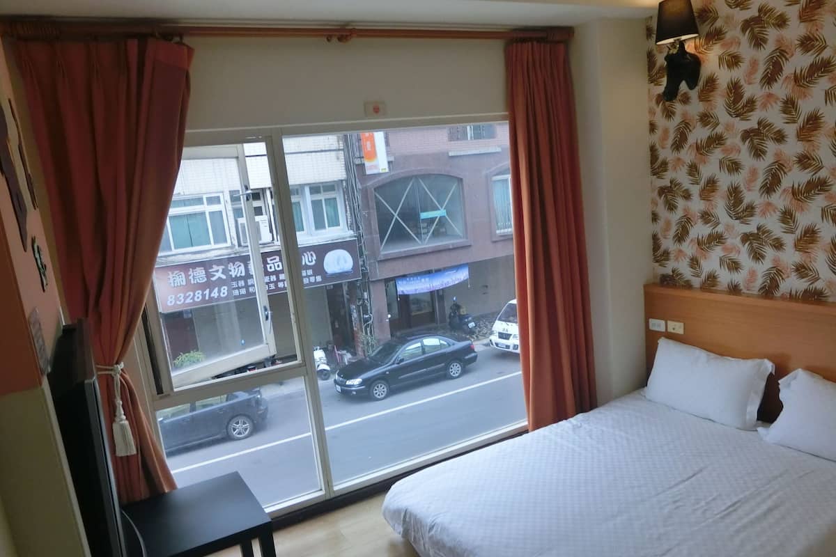 A hotel room with a large bed, a desk, and a window with curtains.